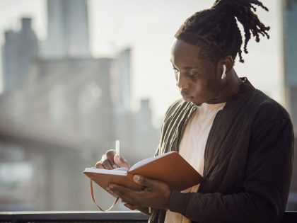 Young man listening to music and writing outdoors